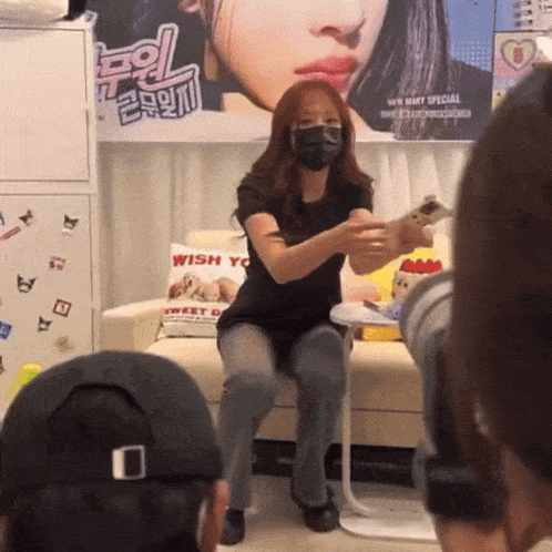 a woman wearing a mask is sitting on a couch in front of a poster that says wish you