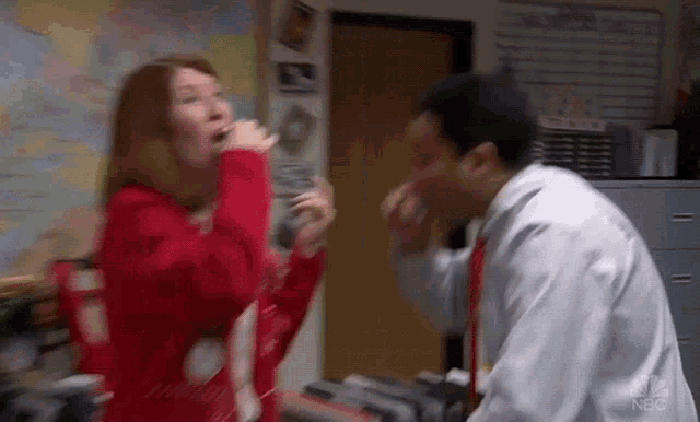 a woman in a red sweater is singing into a microphone next to a man in a white coat .