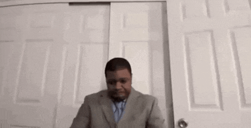 a man in a suit and tie is standing in front of a closet door .