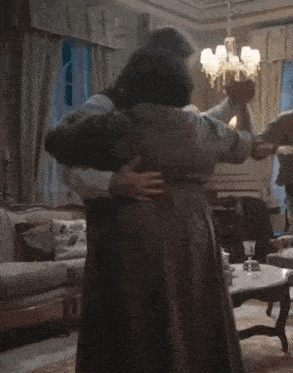 a man and woman are dancing in a living room with a table in the background
