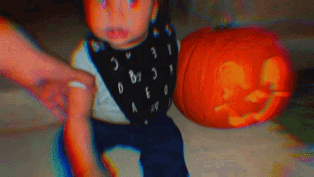 a baby wearing a bib is sitting next to a pumpkin .