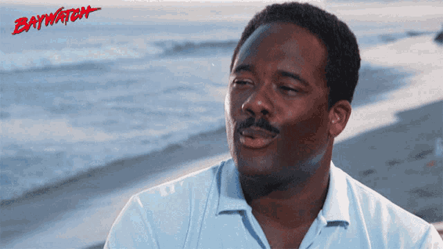 a man sitting on the beach with the word baywatch on the bottom right