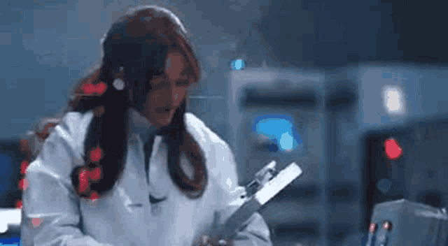 a woman in a lab coat is holding a clipboard in a room .