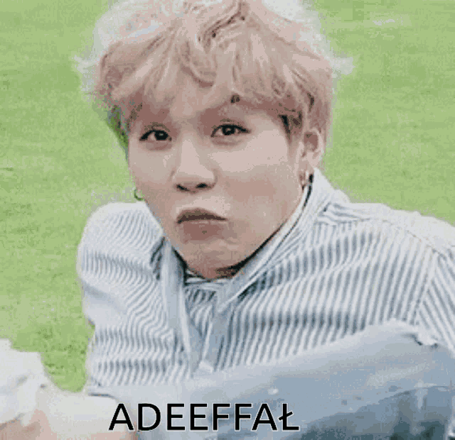 a man in a striped shirt is sitting on a chair in the grass with the word adeffal written on the bottom .