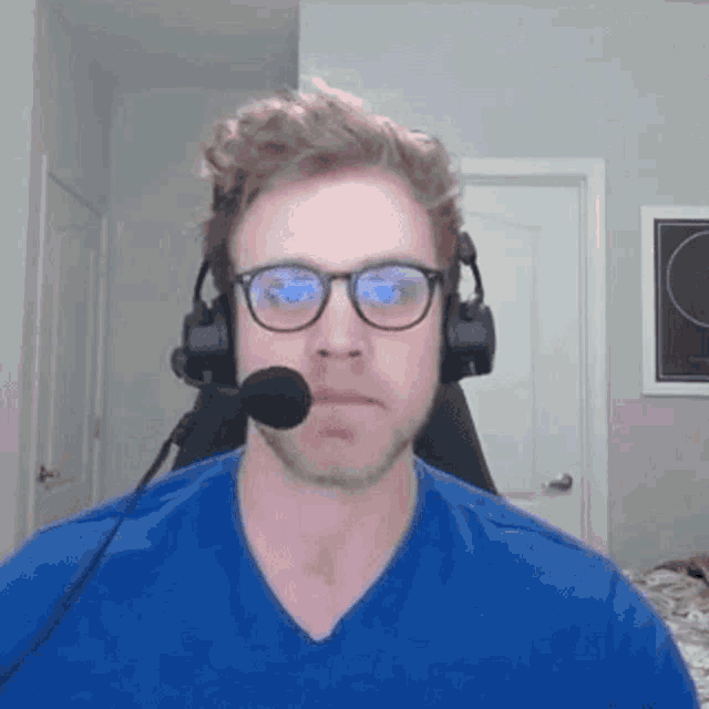 a man wearing headphones and glasses is sitting in a chair with a microphone in his mouth .