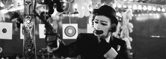 a black and white photo of a clown holding a gun in a carnival .