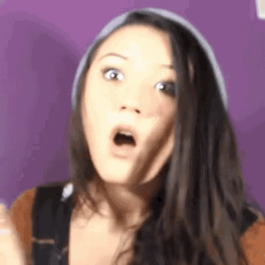 a woman with a surprised look on her face is wearing a beanie .