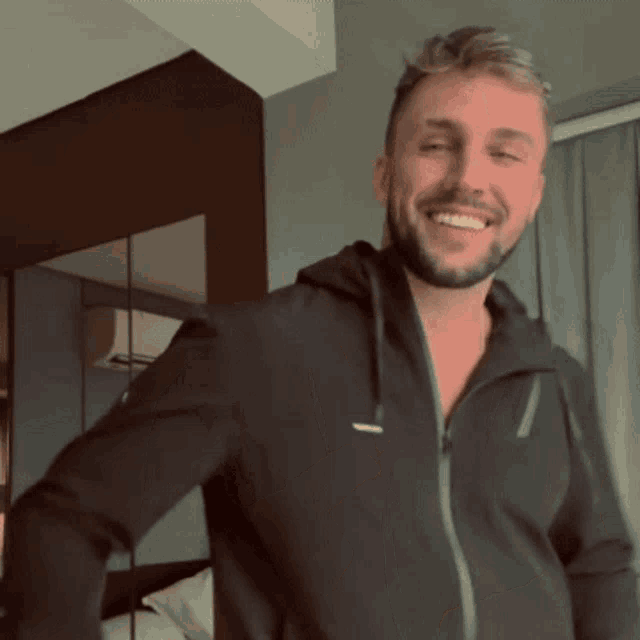 a man with a beard is smiling and wearing a black hoodie