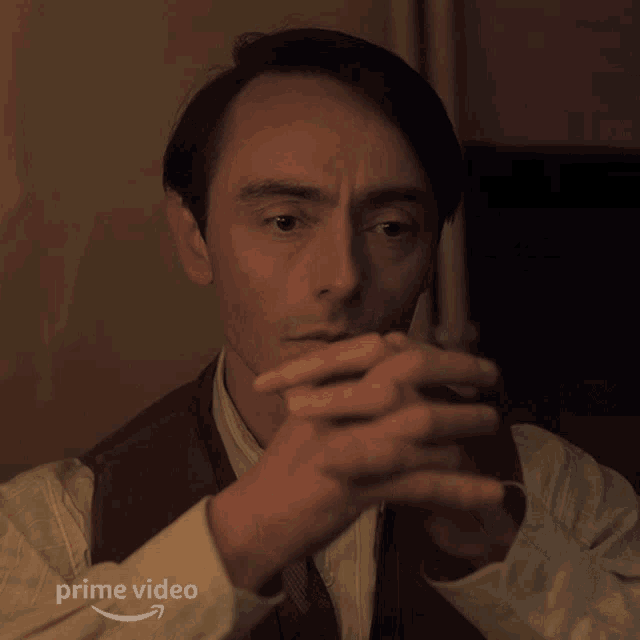 a man with his hands folded in front of his face and the words prime video on the bottom right