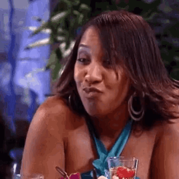 a woman is sitting at a table with a glass of wine and making a face .
