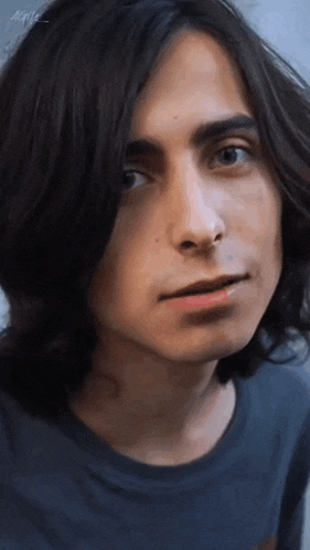 a close up of a young man 's face with long hair and a blue shirt .