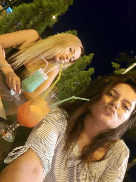 two women sitting at a table drinking cocktails with straws in them