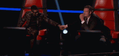 a man in a suit holds another man 's hand while sitting in a chair