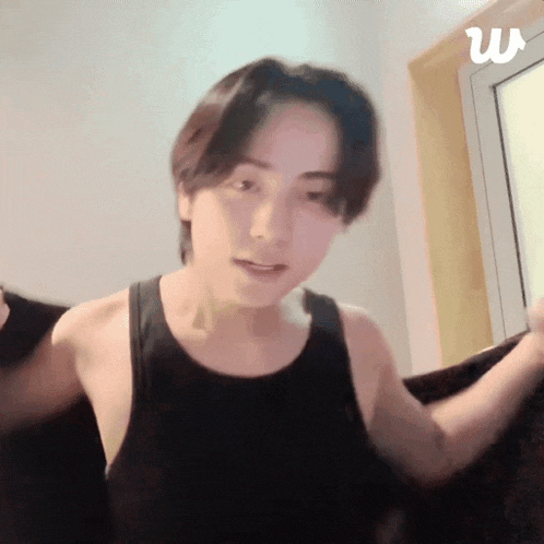 a man in a black tank top is standing in front of a window