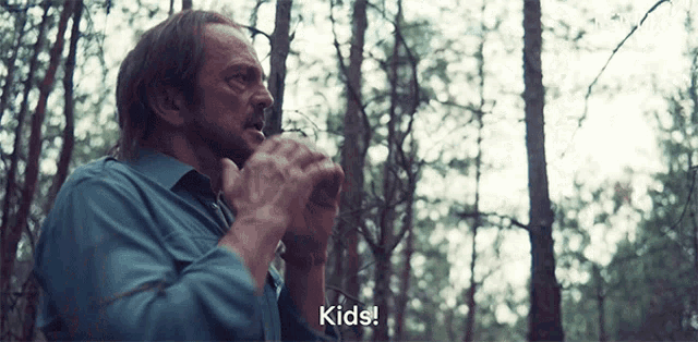 a man in a blue shirt is standing in a forest and says kids
