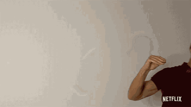 a man in a maroon shirt is standing in front of a white wall and flexing his muscles .
