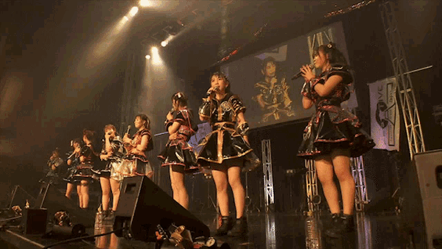 a group of girls singing on a stage in front of a screen