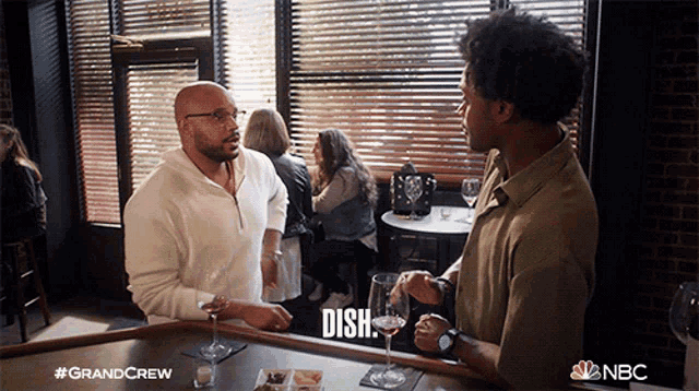 two men are sitting at a bar and one of them is holding a glass of wine and says dish
