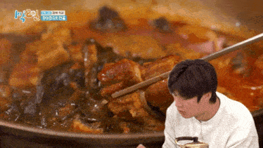 a man is eating a large piece of meat with chopsticks in front of a pot of food