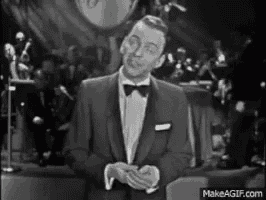 a man in a tuxedo and bow tie is singing into a microphone .
