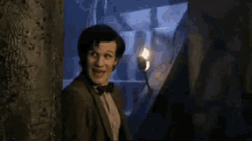 a man in a suit is holding a torch in his hand and covering his mouth .