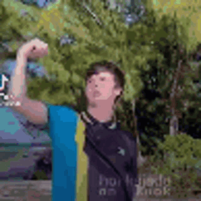 a young man is flexing his muscles while standing in front of a tree .
