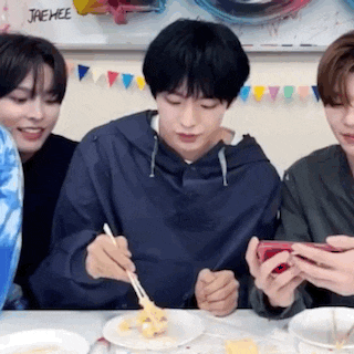 a group of people are sitting at a table eating food and looking at their cell phones .
