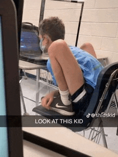 a young boy wearing a mask is sitting on a desk in a classroom .