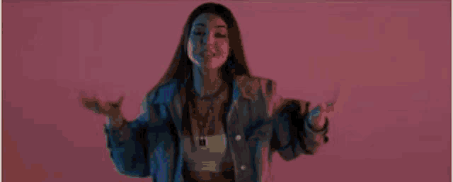 a woman in a blue denim jacket is standing in front of a pink background .