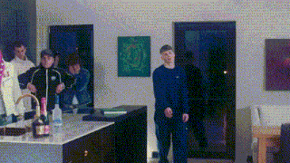 a group of people are standing around a kitchen counter with a bottle of champagne on it