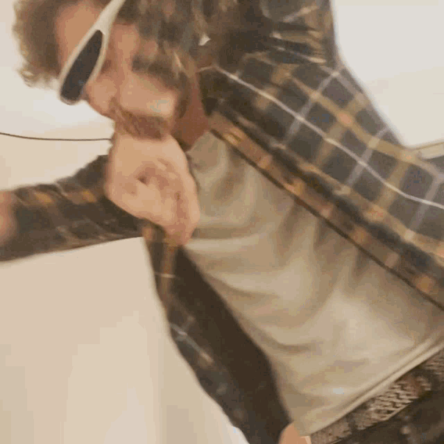 a man wearing sunglasses and a plaid shirt is holding something