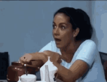 a woman is sitting at a table with a spoon in her hand and a surprised look on her face .