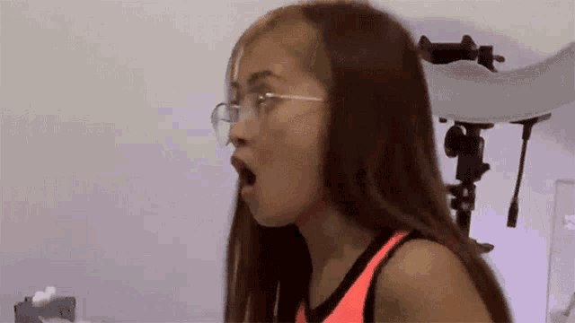 a woman wearing glasses and a pink tank top is making a funny face .