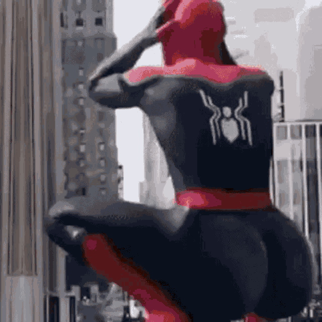 a man in a spiderman costume is squatting down in front of a city .