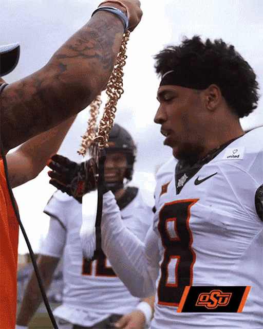 a football player with the number 8 on his jersey is being presented with a gold chain