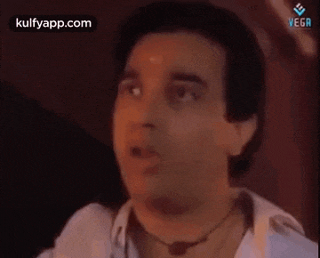 a man with a necklace around his neck is making a funny face while talking to someone .