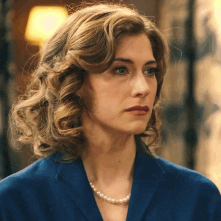 a woman in a blue jacket and pearl necklace