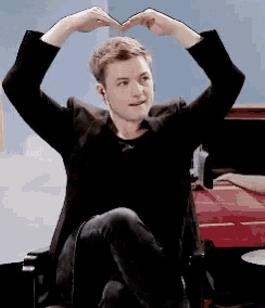 a man in a black jacket is making a heart shape with his hands