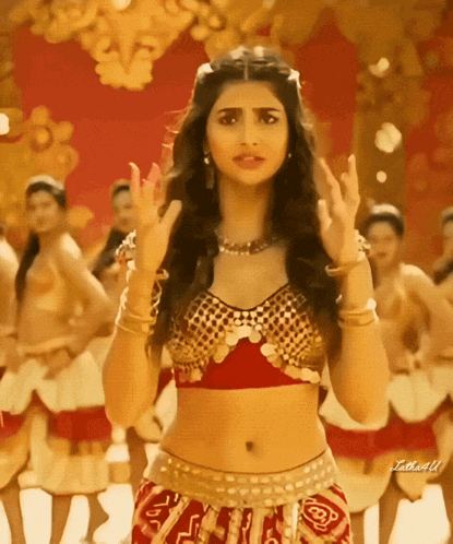 a woman in a gold top and red skirt is dancing in front of a group of women