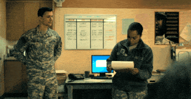 a man in a military uniform stands next to a woman in a military uniform who is looking at a piece of paper