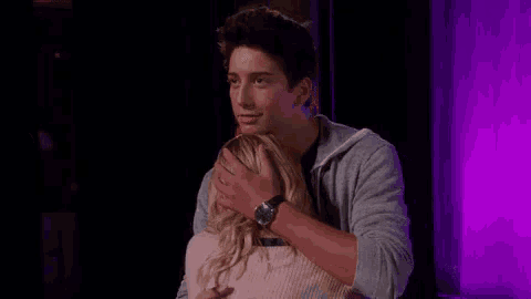 a young man is hugging a young woman in a room with purple lights .