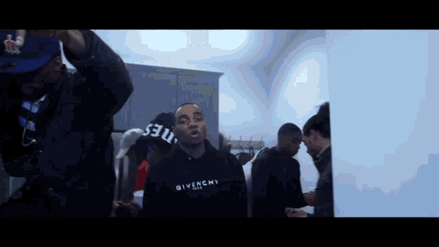 a man in a givenchy hoodie stands in a crowd