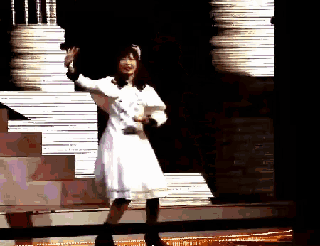 a woman in a white dress is waving her hand