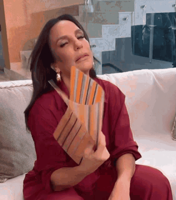 a woman in a red dress is sitting on a couch holding a fan in her hand .