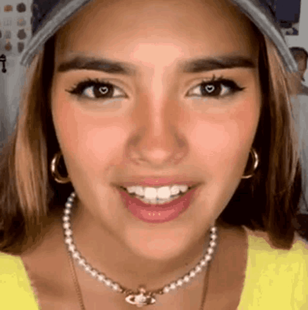 a close up of a woman wearing a hat , pearl necklace and hoop earrings .