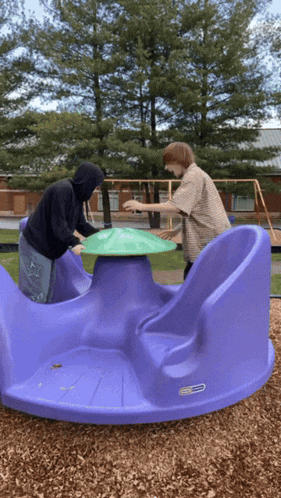 two boys play on a purple merry go round