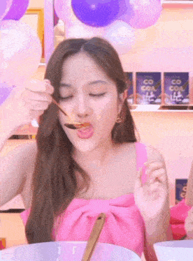 a woman in a pink dress is eating with a spoon .