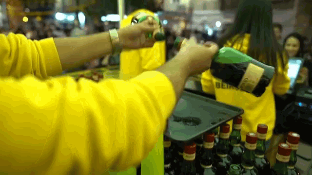 a man in a yellow shirt pours a bottle of alcohol into a tray