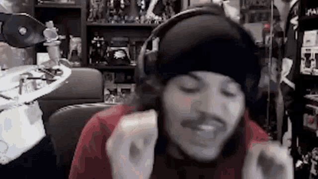 a man wearing headphones and a beanie is eating a sandwich in a room .
