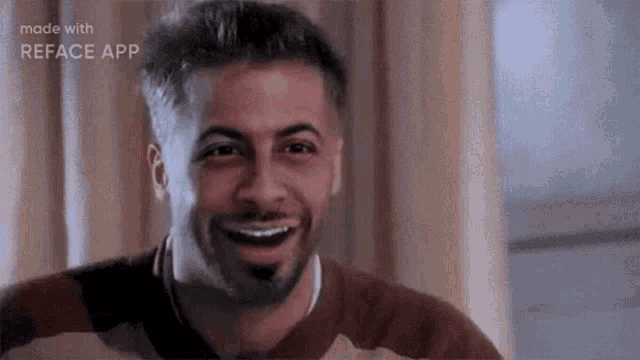 a man with a beard is smiling and looking at the camera while sitting in front of a window .